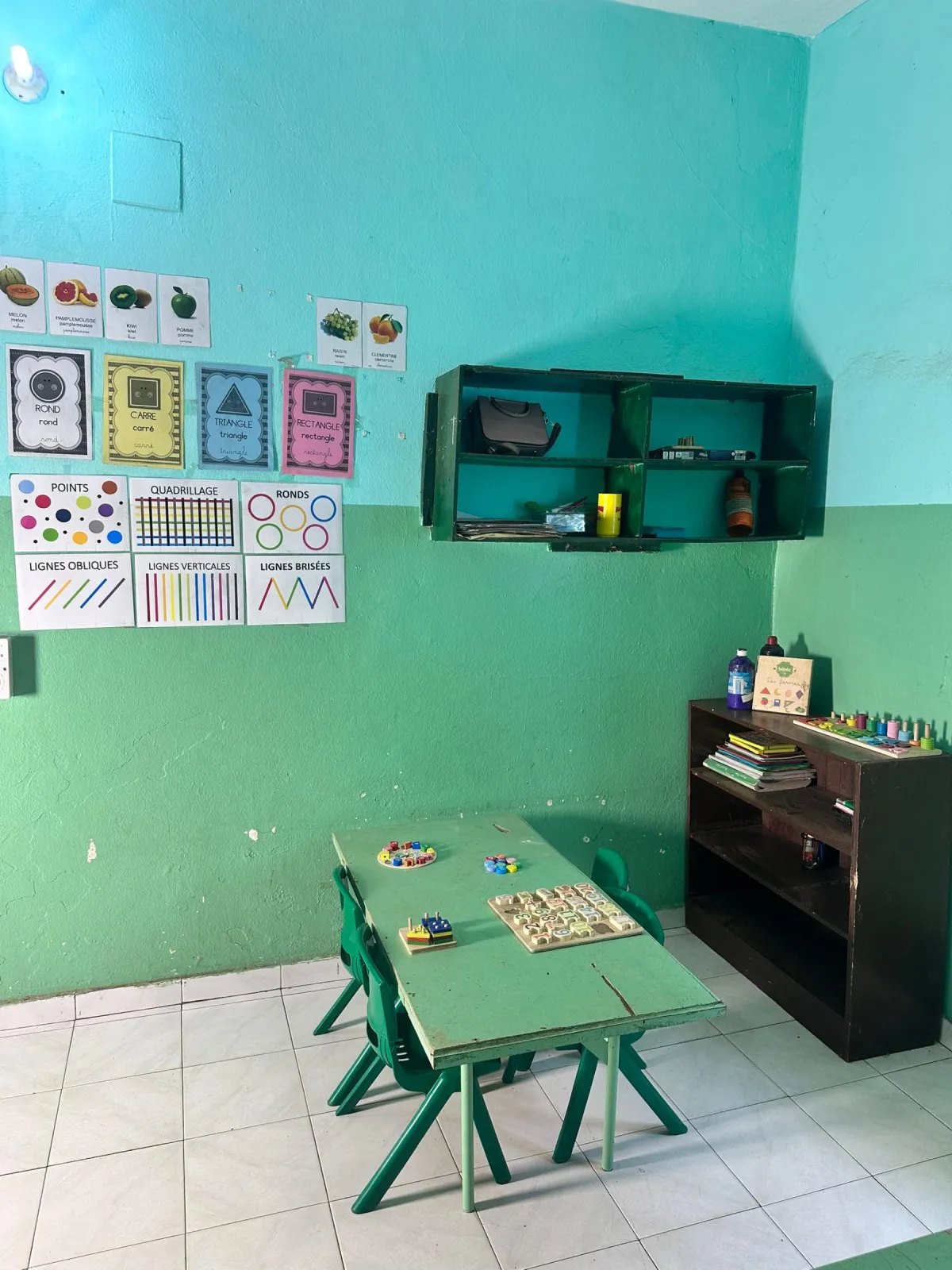 Coin d'apprentissage avec affiches des formes (rond, carré, triangle, rectangle), des fruits et des lignes, table et jeux éducatifs