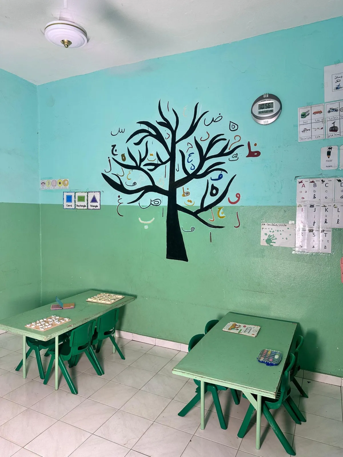 Tables d'activités avec puzzles de lettres et peinture, devant l'arbre de l'alphabet arabe