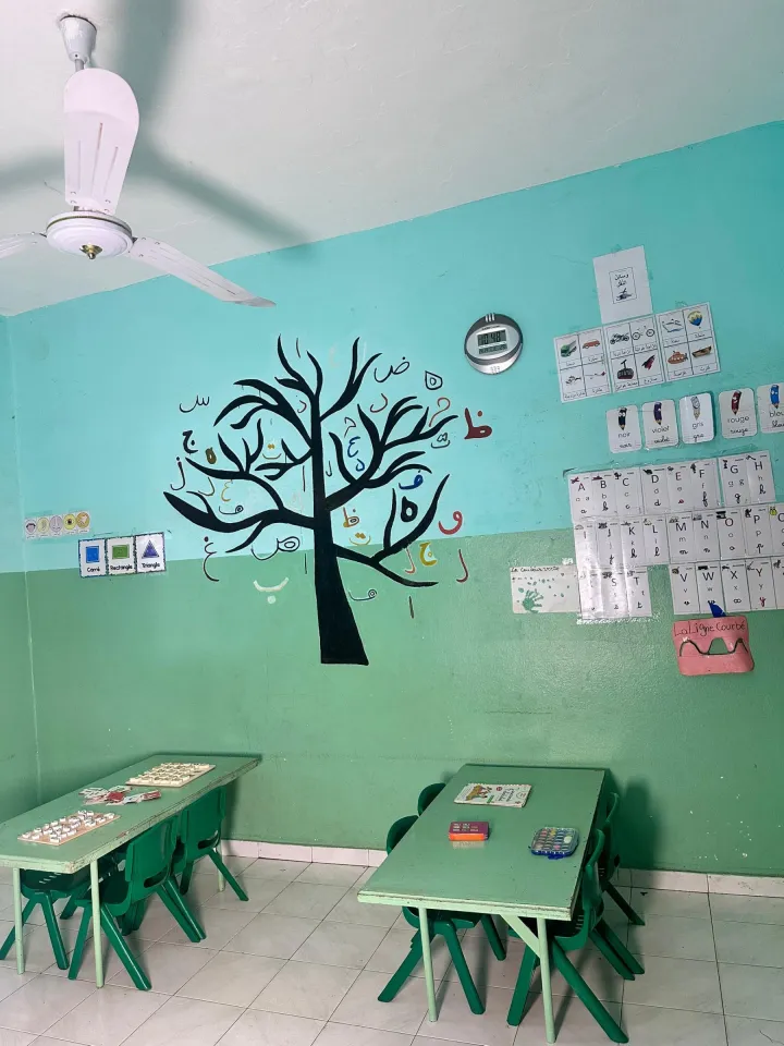 Salle de classe avec un arbre peint au mur entouré des lettres de l'alphabet arabe, l'alphabet français affiché à côté